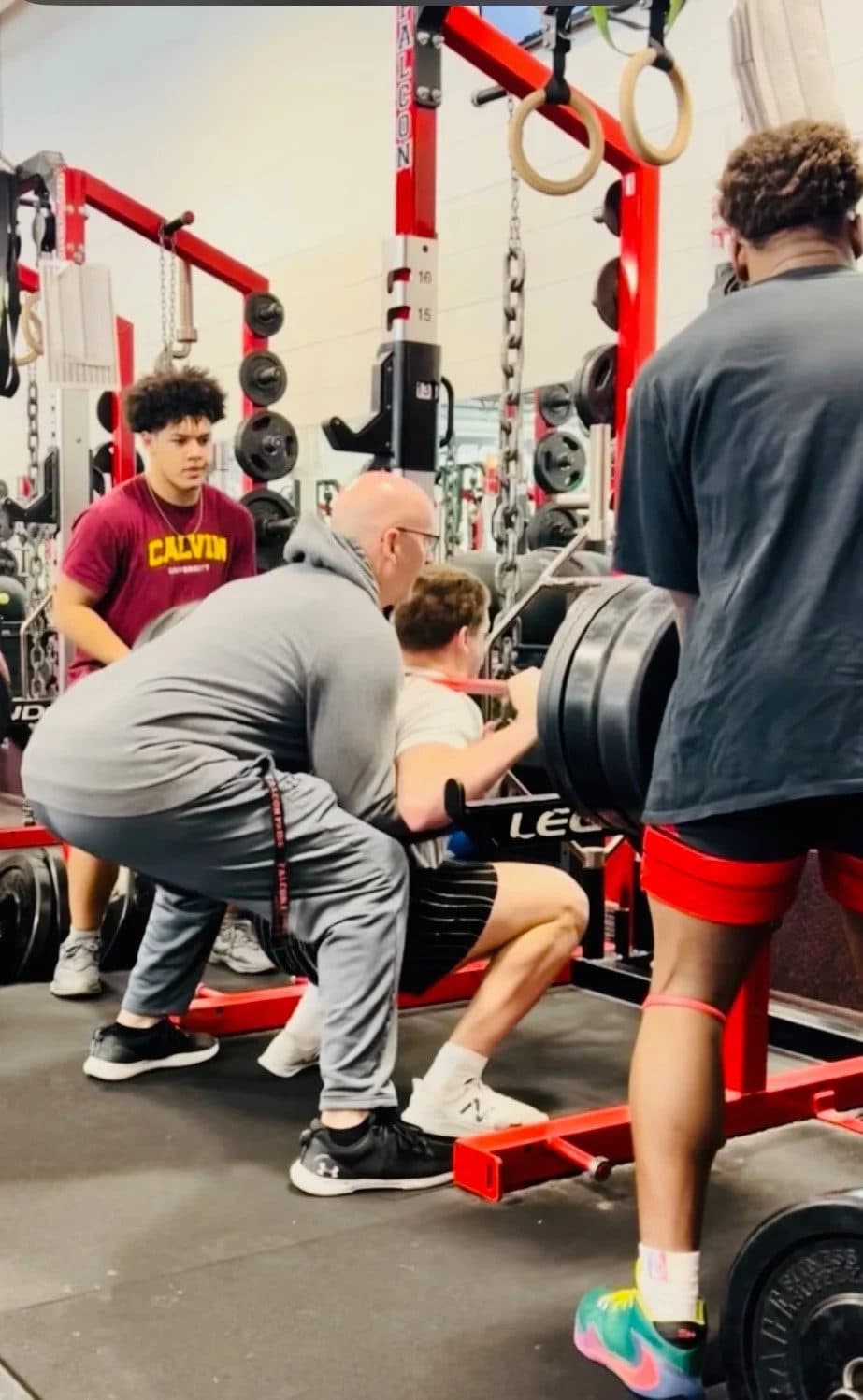 Coach Martens spotting an athlete through a loaded squat while teammates watch